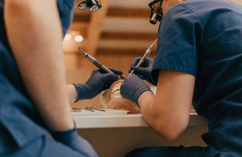 Clinicians in loupes working on a dental training manikin at a bench.